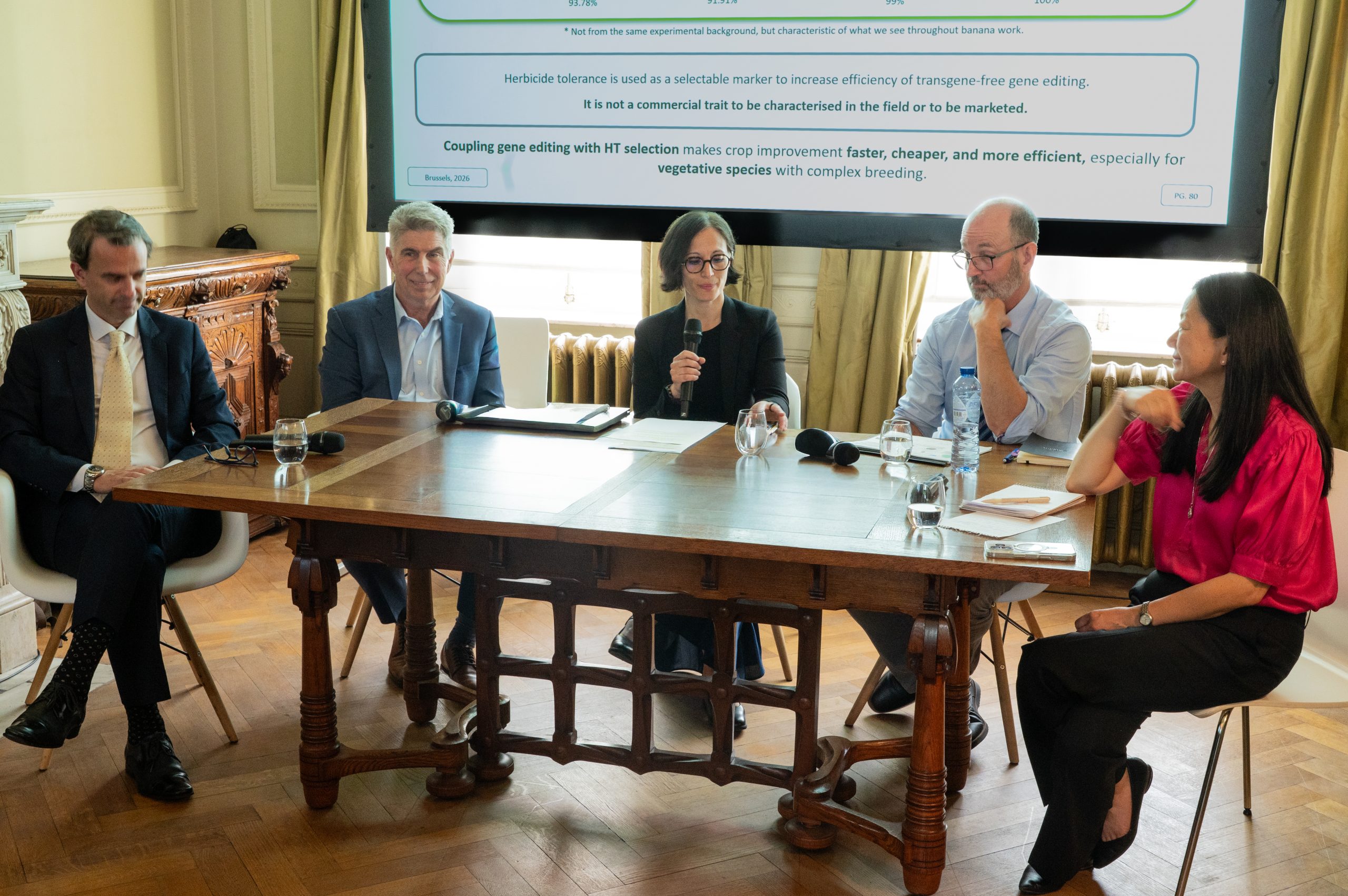 five people sit around a table in professional dress with a screen behind them